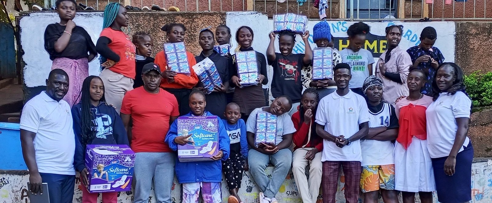 Children at a children's home holding packs of sanitary pads, gathered with the Foundation team for a group photograph.