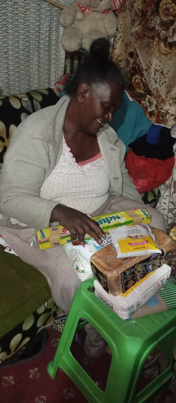 A widow smiling as she receives her monthly food support of flour, bread, milk and cooking fat at home.