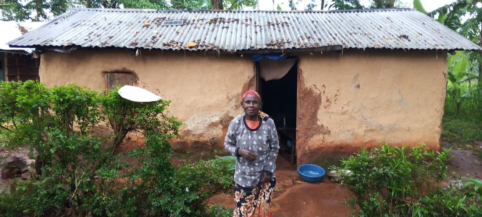 A widow supported by the Foundation standing outside her mud-walled home.