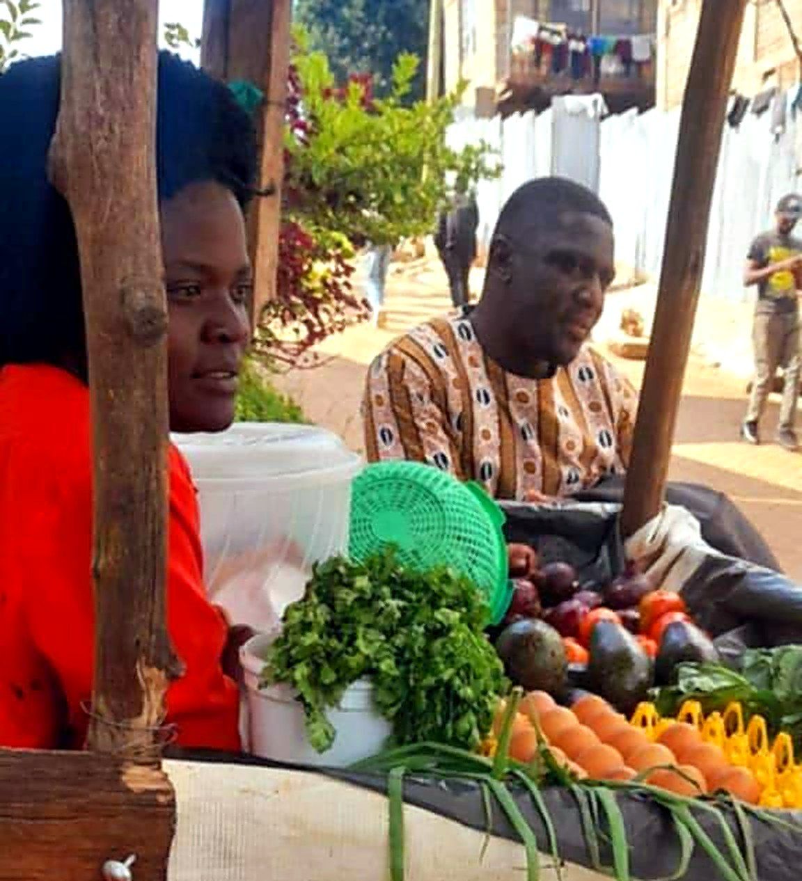 A woman at her fruit and vegetable stall of avocados, tomatoes, greens and eggs, with a Foundation team member beside her.