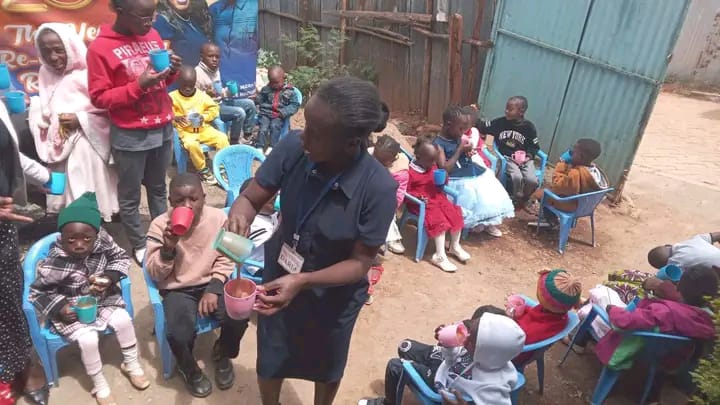 Children seated on plastic chairs in a church compound being served porridge in cups at a Sunday-morning feeding session.