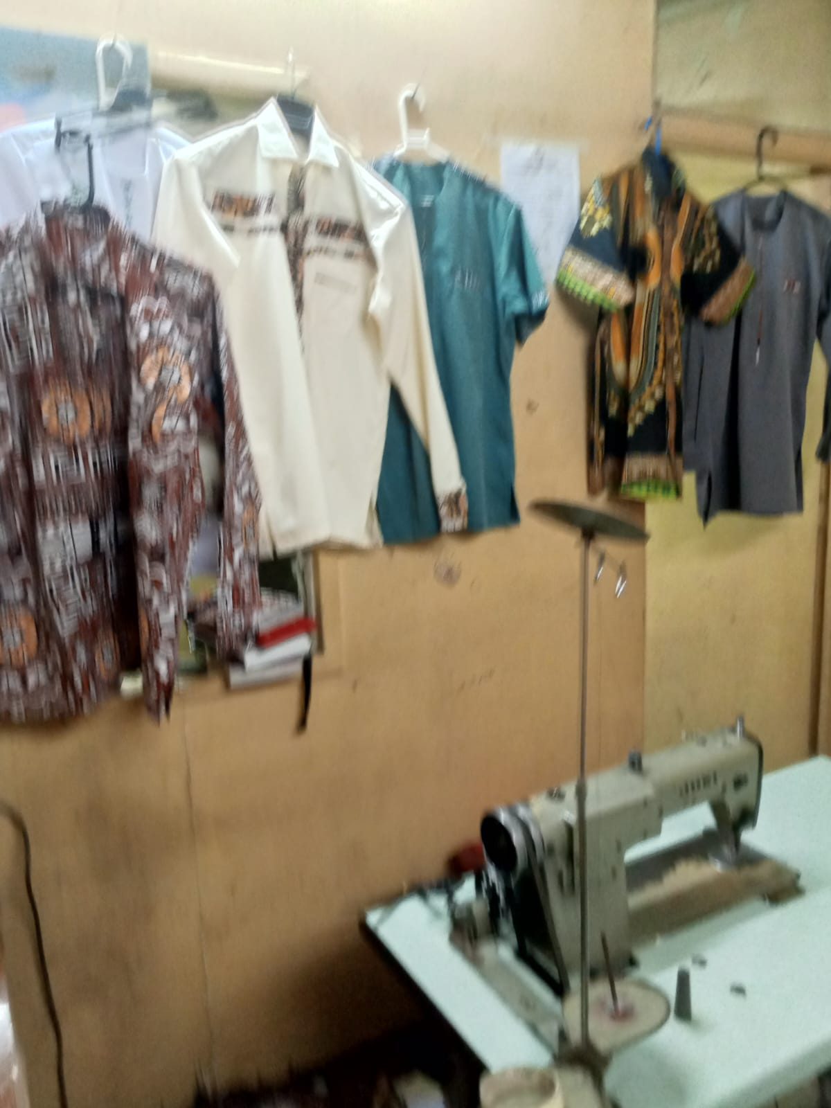Before: Mr Owino's small tailoring corner at home, with a single sewing machine and a few finished shirts hanging on the wall.
