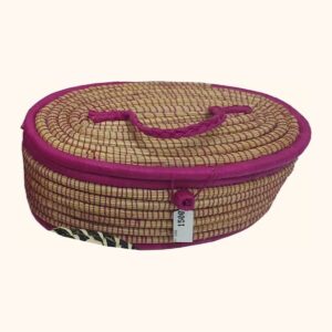 An oval coiled natural-fibre box with a fitted lid, pink trim, a plaited pink handle and a knotted button.