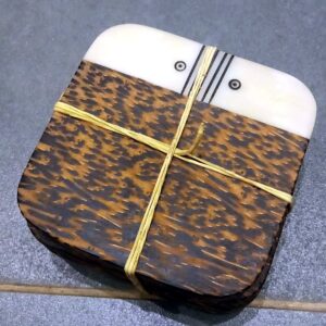 A tied stack of square coconut wood coasters with a cream inlaid band decorated with black lines and circles.
