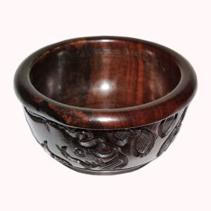 A small round polished dark wood bowl with a band of carved elephant and leaf designs around the outside.
