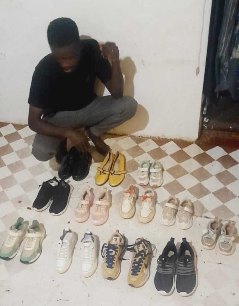 A young man crouching beside rows of donated children's shoes laid out for distribution.