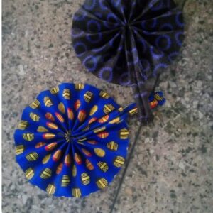 Two round folding hand fans made from pleated Ankara fabric, one royal blue with yellow and red print and one dark purple with blue rings.