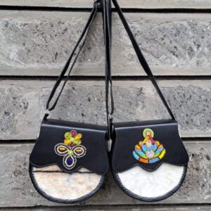 Two round black leather crossbody bags with scalloped flaps, beaded flower motifs and natural cowhide fronts, hanging by their straps.