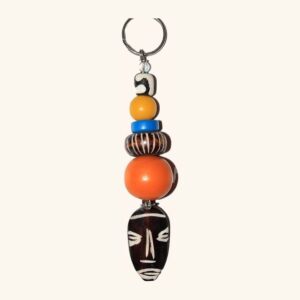 A key ring strung with bone, yellow, blue, carved and orange beads, finished with a small carved mask pendant.