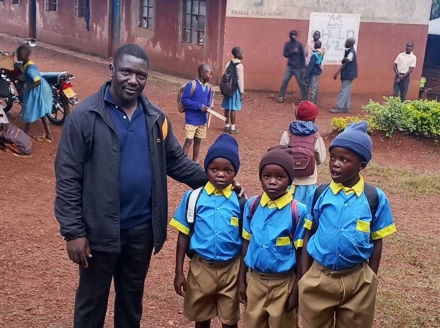 Three boys in new school uniforms standing with the Executive Director outside their school.