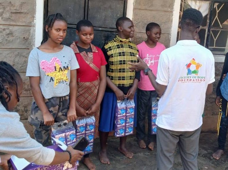 Girls receiving packs of sanitary pads from Foundation staff during a door-to-door distribution.