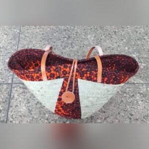 A woven palm raffia tote lined and panelled with orange and black Ankara fabric, with tan leather handles and a leather button fastening.