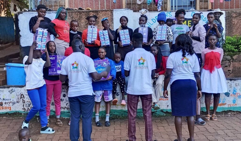 Foundation team members in Cistern of Hope Foundation branded T-shirts handing out sanitary pads to children at a children's home.