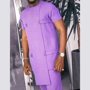 A man wearing a lilac short-sleeved kaftan with a round neck, an asymmetric layered hem and buttoned fabric tabs across the front, with matching trousers.