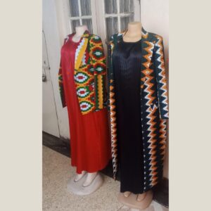 Two outfits on mannequins: a long red pleated dress under a short African print blazer in yellow, green, red and white, and a long black pleated dress under a full-length coat in a dark green, orange and white zigzag print.