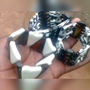 Handcrafted stretch bracelets held in a hand: one of chunky white and dark brown cow bone pieces, and several multi-row bracelets of black and white batik-patterned bone tubes with black beads.