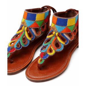 A pair of tan leather thong sandals with a high beaded ankle cuff in blocks of blue, yellow, orange and green and a cascading teardrop pattern of colourful beadwork down the foot.
