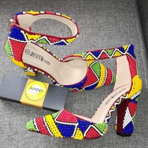 A pair of pointed-toe block-heel shoes with ankle straps, fully covered in handmade beadwork in red, yellow, blue, green and white geometric patterns.