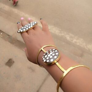 Design 1: a brass hand bracelet worn on the wrist, with a round black batik cow bone disc dotted in white on the back of the hand, joined to a brass ring with a matching oval bone top.