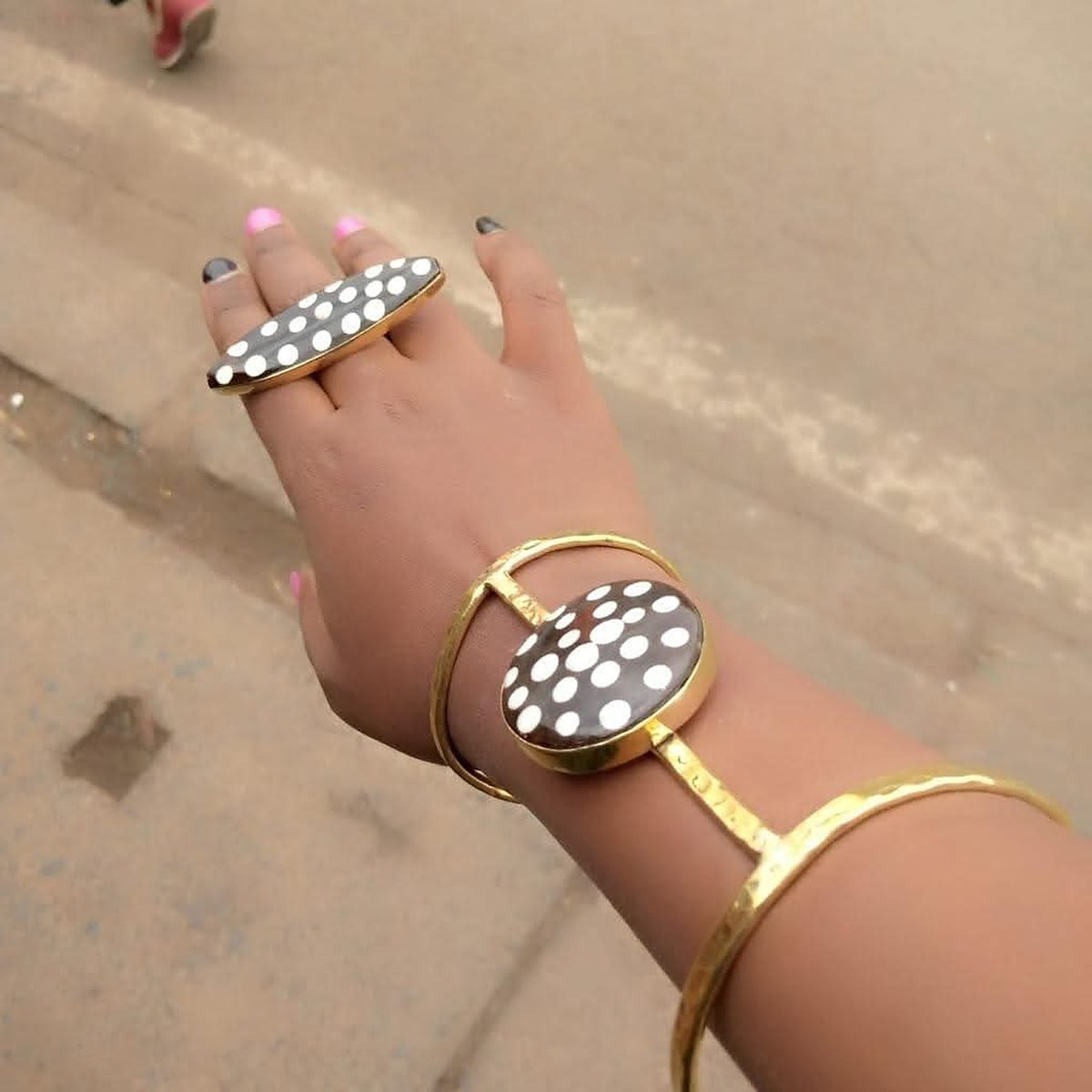 African Batik Cow Bone and Brass Cuff Bracelet 1 Design 1: a brass hand bracelet worn on the wrist, with a round black batik cow bone disc dotted in white on the back of the hand, joined to a brass ring with a matching oval bone top.