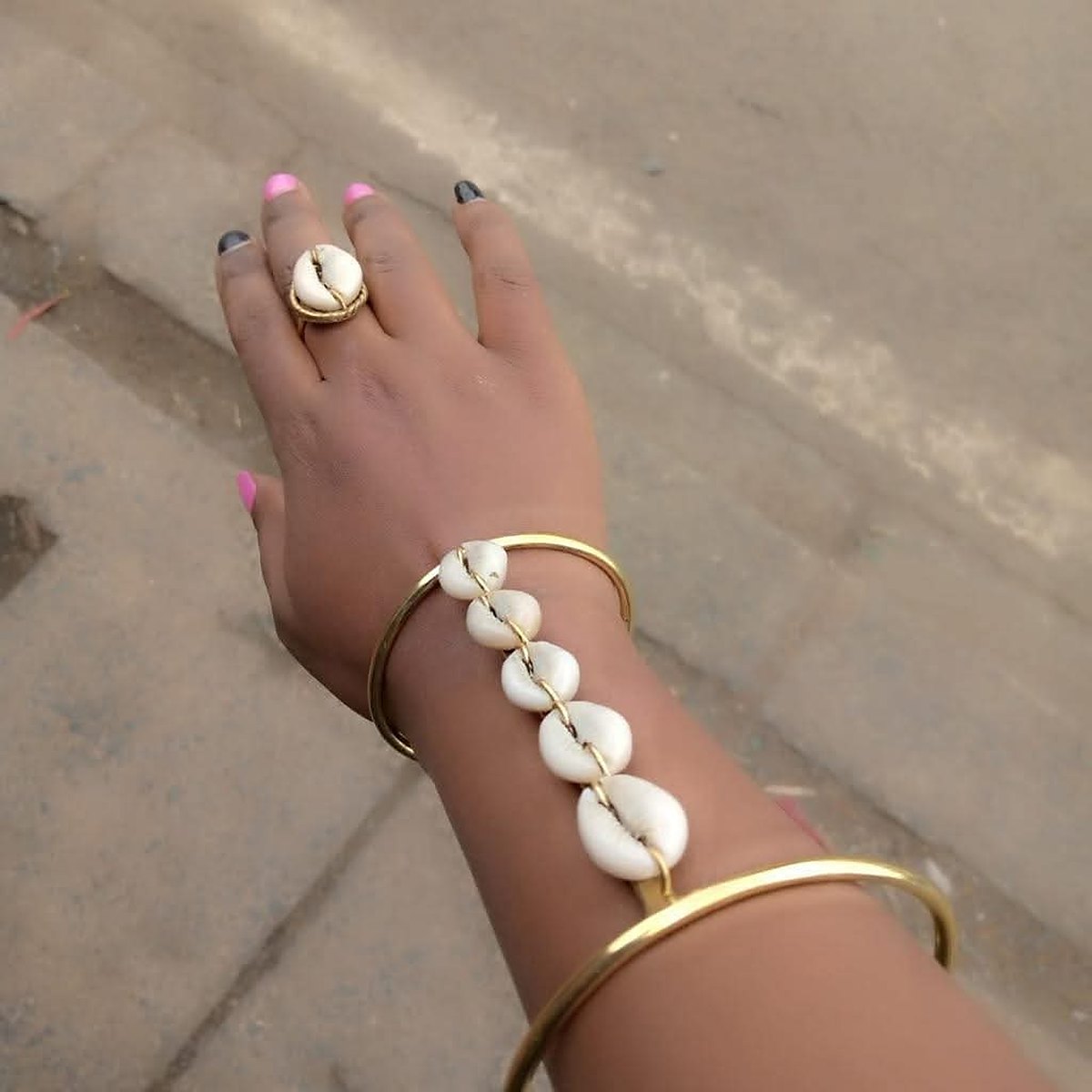 African Batik Cow Bone and Brass Cuff Bracelet 2 Design 2: a brass bangle worn on the wrist with a chain of white cowrie shells running to a brass ring set with a cowrie shell.
