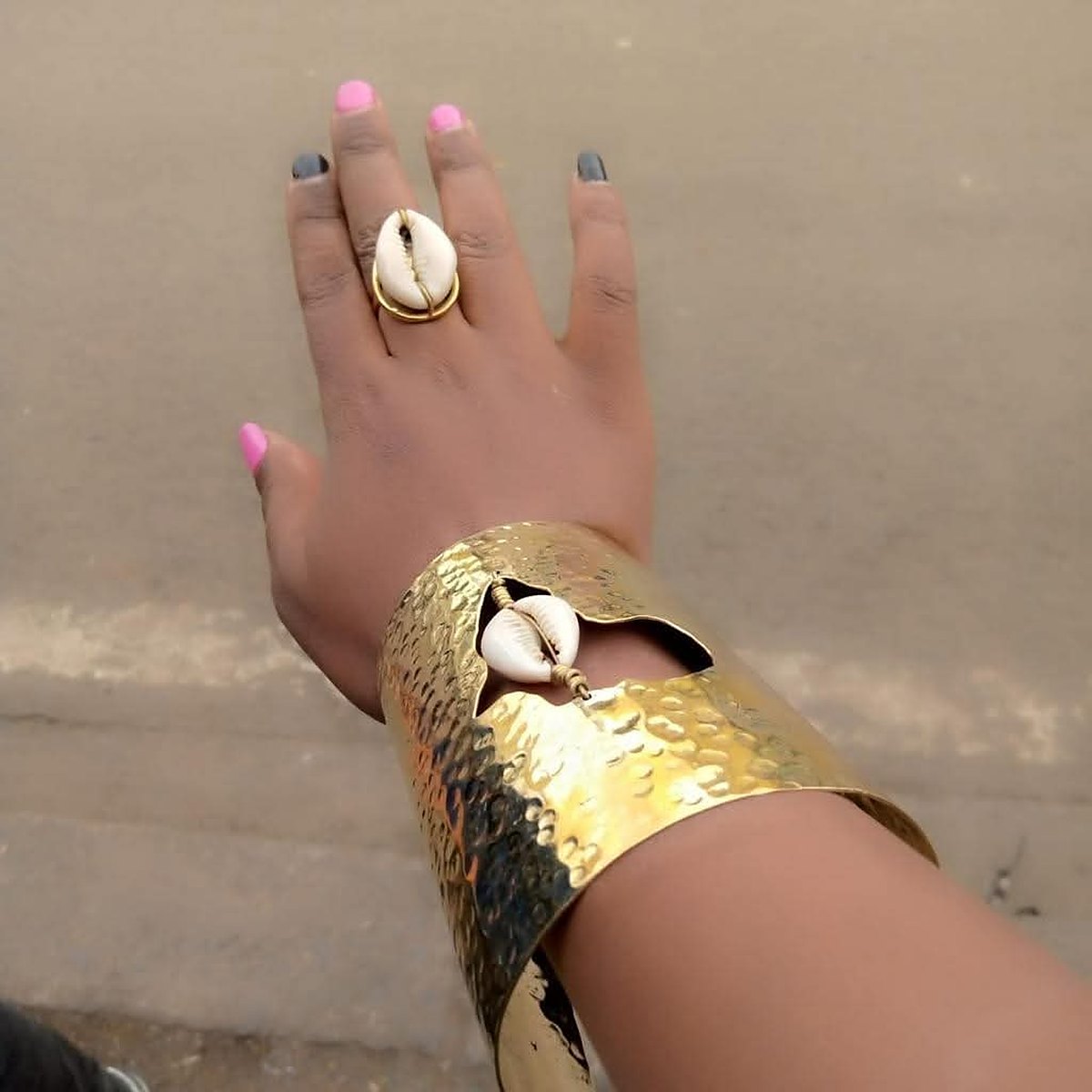 African Batik Cow Bone and Brass Cuff Bracelet 3 Design 3: a wide hammered brass cuff worn on the forearm with a cut-out set with a white cowrie shell.