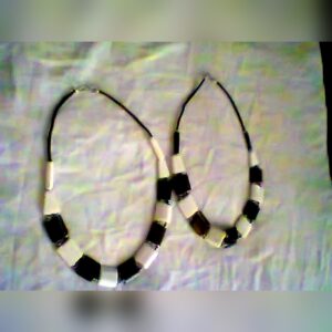 Two handmade chunky necklaces of alternating black and white rectangular beads on black cords, laid out on a light cloth.