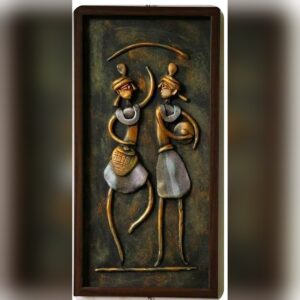 A framed 3D clay relief of two tall tribal dancers in bronze and silver tones, one dancing and one holding a drum, on a dark textured background in a brown wooden frame.