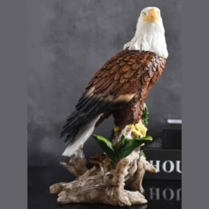 A hand-painted sculpture of a bald eagle with a white head and rich brown feathers, perched on a carved wood-effect branch with green leaves and yellow flowers.