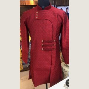 A maroon Indo-Western sherwani on a mannequin, in a tonal diamond-patterned fabric with a mandarin collar, an asymmetric curved front panel and gold buttons on three fabric tabs at the waist.