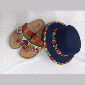 A navy felt hat with colourful Maasai beadwork around the crown and brim edge, beside a pair of brown leather toe-loop sandals with matching beaded straps.