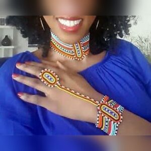 A woman wearing a matching Maasai beaded set: a choker in bands of blue, red, yellow and white, and a hand piece joining a beaded wristband to a beaded finger ring.
