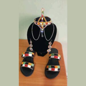 A matching Maasai beaded set: a beaded collar necklace with silver chains and a long beaded pendant, a pair of three-tier beaded drop earrings, and black sandals with two beaded straps in orange, green, red, white and black.