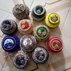 A collection of round lidded jewellery boxes covered in Maasai beadwork, in multicolour, red, yellow, green, blue, black and gold designs with beaded swirl motifs on the lids.