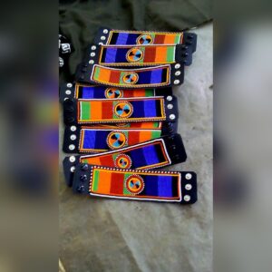 A row of black leather cuff bracelets with snap fasteners, each beaded in bands of blue, red, orange and green with a round beaded medallion in the centre.