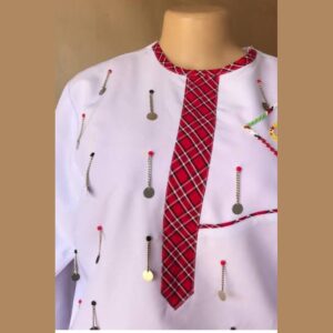 A white round-neck shirt on a mannequin with a red checked Maasai shuka placket and neckline, a curved red check pocket trim, beaded details and rows of hanging silver chains with discs.