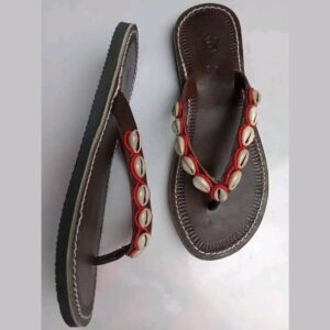 A pair of dark brown leather thong sandals with stitched edges, the straps decorated with white cowrie shells set in red beadwork.