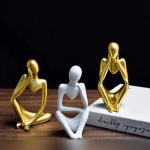 Three abstract seated thinker figurines, two in glossy gold and one in matte white, each resting its head in its hands.
