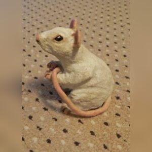 A handmade white polymer clay mouse sitting up with dark eyes, pink ears and a long pink tail curled around its body.