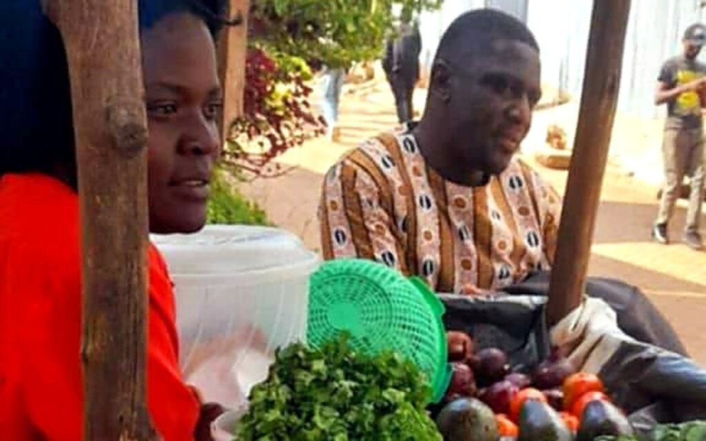 A woman at her fruit and vegetable stall with a Foundation team member beside her.