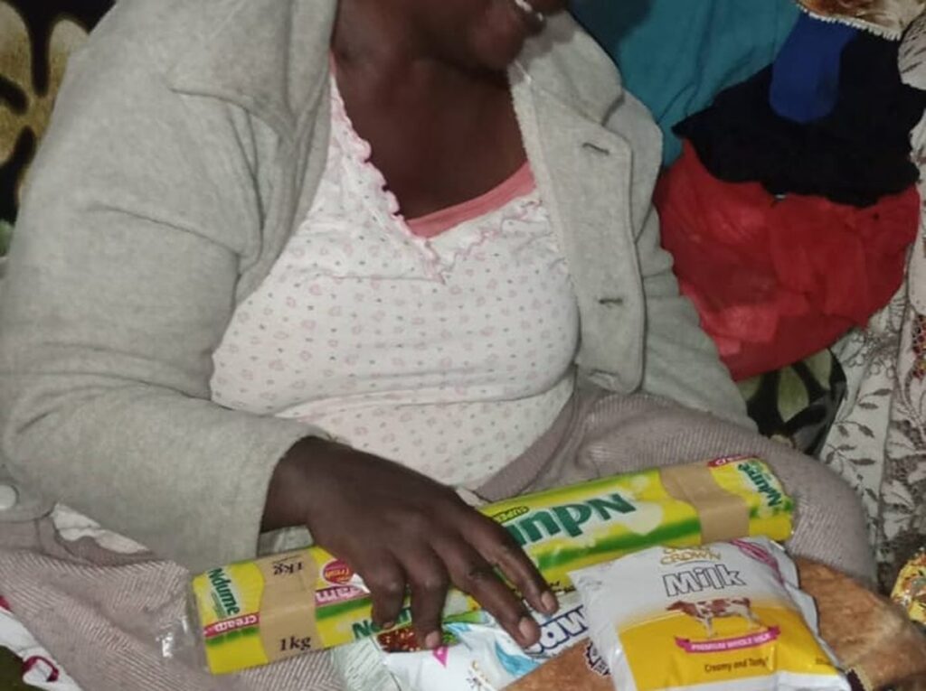 A widow smiling as she receives her monthly food support of flour, bread, milk and cooking fat at home.